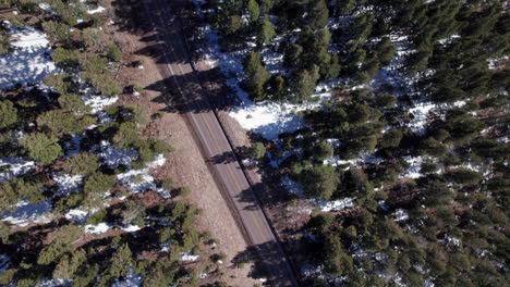 Top-down-view-of-a-snowy-mountain-road-in-the-forest-surrounded-by-pine-trees,-drone-shot