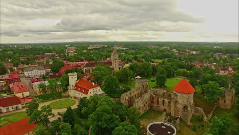 Aerial-View-of-Cēsis-Castle-Capturing-the-Iconic-Medieval-Fortress-and-Surrounding-Townscape-in-Latvia's-Daylight,-Amidst-Cloudy-Skies
