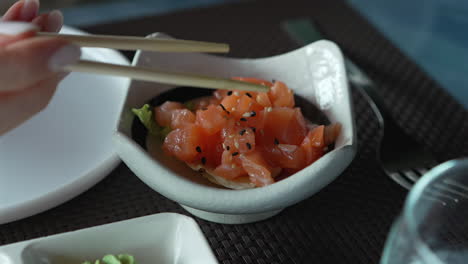 A-woman-with-chopsticks-in-hand-takes-a-piece-of-salmon-tartare-with-sesame-and-herbs