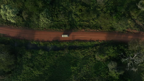 Tour-truck-driving-down-National-Park-dirt-road-in-Uganda,-Africa