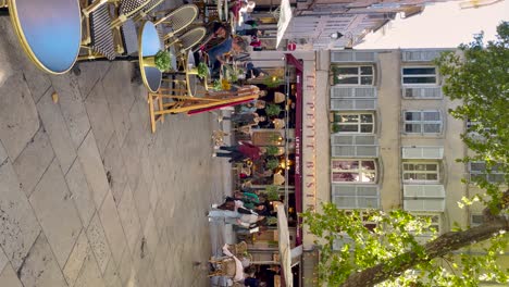People-walk-by-restaurants-on-square-in-Aix-en-Provence,-vertical-shot