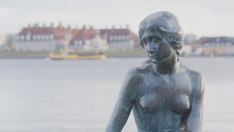 Close-up-frontal-on-iconic-The-Little-Mermaid-statue-with-boat-passing-in-back