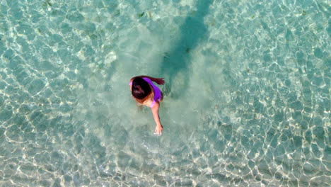 A-woman-in-a-pink-swimsuit-enjoys-making-circles-in-the-turquoise-sea,-captured-in-aerial-top-down-view