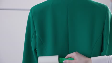 Woman-Using-Lint-Roller-On-Back-Side-Of-Green-Suit-At-Laundry-Shop