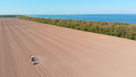 Aéreo:-Tractor-Arando-El-Campo-Junto-Al-Mar-En-El-Norte-De-Alemania-En-Un-Día-Soleado