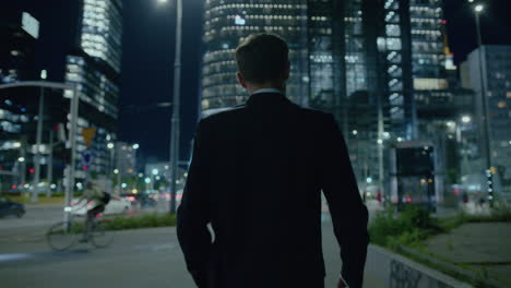 Elegant-young-male-in-suit-strolling-at-night-in-modern-illuminated-city
