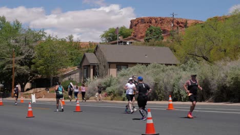 People-running-and-racer-biking-in-front-of-house-and-red-landscape-at-the-Intermountain-Health-IRONMAN-70