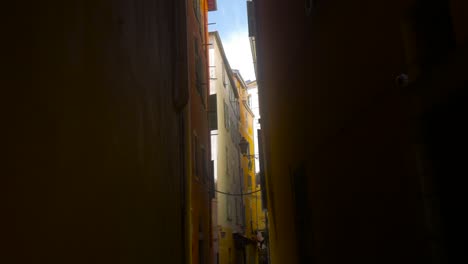 Traditional-Narrow-Alley-from-Italian-Heritage-in-the-South-of-France-and-Clothes-Hanging-from-Green-Orange-and-Red-Buildings-during-the-Day-with-Bright-Sunlight