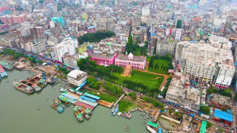 Famous-palace-Ahsan-Manzil-on-the-Buriganga-river,-cargo-ships-moored,-aerial