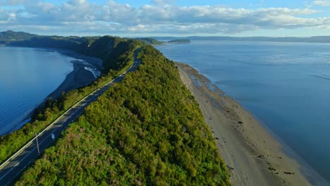 Coastal-road-curving-along-Lemuy-Island's-shore-with-fishing-nets,-Chiloe,-aerial-view