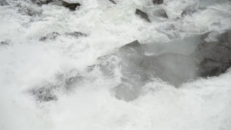 Close-tracking-shot-of-majestic-waterfalls-careening-over-river-rocks-forming-white-water-rapids