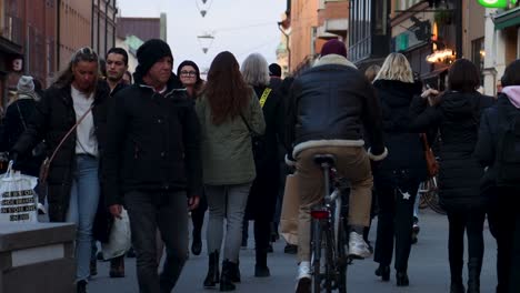 Man-on-bike-and-weekend-shoppers-on-street-in-Stockholm,-slow-motion