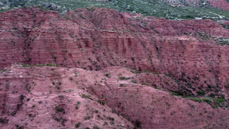 Sedimentary-rock-cliffs-rich-in-iron-oxide-glow-red,-Argentina-aerial