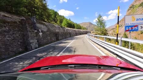 POV-Of-Car-With-Red-Bonnet-Driving-Along-Scenic-Mount-Cenis-Road-In-France-On-Sunny-Day-Past-Mountain-Cliffs-And-Hills