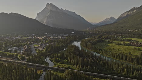 Banff-AB-Canada-Aerial-v32-flyover-forested-valley-capturing-quaint-town-along-Bow-river-and-views-of-Rundle-mountain-ranges-with-train-riding-across-the-scene---Shot-with-Mavic-3-Pro-Cine---July-2023