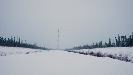 Statische-4K-Teleaufnahme-Einer-Funkantenne-Eines-Stromnetzes-Am-Ende-Einer-Verschneiten-Winterstraße-Zwischen-Waldbaumreihen