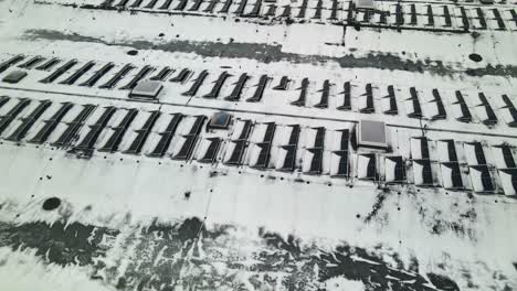 Drone-shot-of-solar-panels-on-a-industrial-building-roof-covered-with-snow-in-winter
