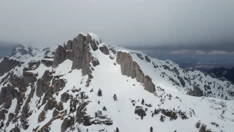 Snow-covered-Ciucas-Mountains-under-a-cloudy-sky,-aerial-view