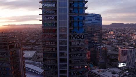 Aerial-rising-close-up-panning-shot-of-the-Oceanwide-Plaza-graffiti-towers-in-downtown-Los-Angeles,-California-at-sunset