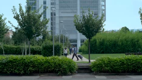 Geschäftsleute-Gehen-Von-Einem-Modernen-Bürogebäude-Mit-Grünen-Bäumen-Und-Blauem-Himmel-Weg