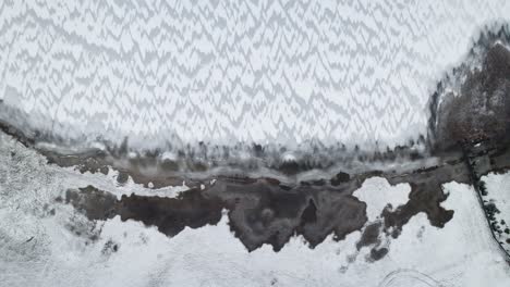 Slow-descend-aerial-bird's-eye-view-of-windswept-ice-covered-snow-lake-in-Suwalki-Gap-Masuria-Poland