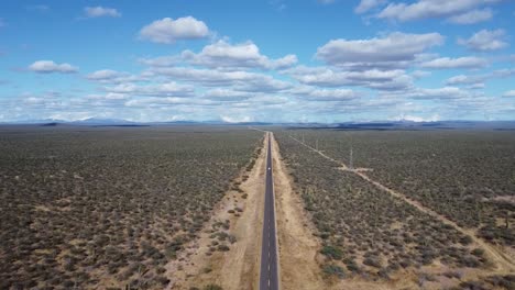 Un-Largo-Camino-Recto-Que-Atraviesa-El-Vasto-Desierto-De-Baja-California-Sur,-Bajo-Un-Cielo-Azul-Con-Nubes,-Vista-Aérea