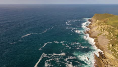 Vuelo-En-El-Mar-Cantábrico-Con-Un-Dron-Donde-Vemos-Un-Acantilado-Con-Forma-De-Península,-Haciendo-Girar-Una-Cámara,-Descubrimos-El-Cielo-Con-El-Mar-En-El-Horizonte-Y-Vemos-Unas-Islas-De-España