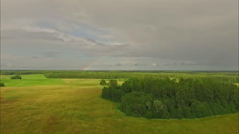 Aerial-view-of-a-colorful-rainbow-at-the-horizon-on-a-cloudy-day-over-a-countryside