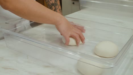 Chef-places-prepared-pizza-dough-balls-into-storage-tray-in-kitchen