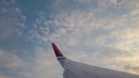Wing-of-Norwegian-airplane-in-sky,-cloudy-sunset-and-distant-coast