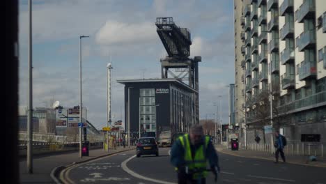 The-Finnieston-crane-in-Glasgow-by-the-River-Clyde-with-peaceful-flow-of-cars-and-cyclist's-passing-by-on-a-calm-sunny-day