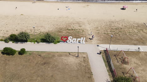 Aerial-View-of-Sarti-Landmark-Sign-by-the-Beach,-Sithonia,-Greece,-Drone-Shot
