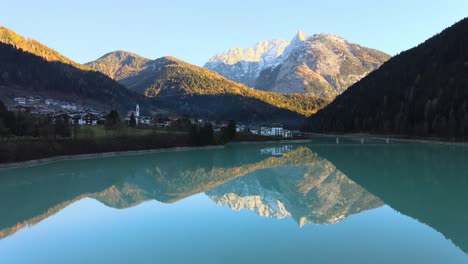 Lake-with-crystal-cear-water-surrounded-by-mountains-and-a-small-town-in-Bellluno,-Italy