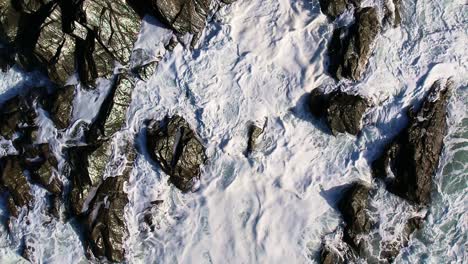 Slow-Motion-Ocean-Waves-and-White-Foam-Crashing-Over-Cornish-Rocks-with-an-Aerial-Top-Down-Shot