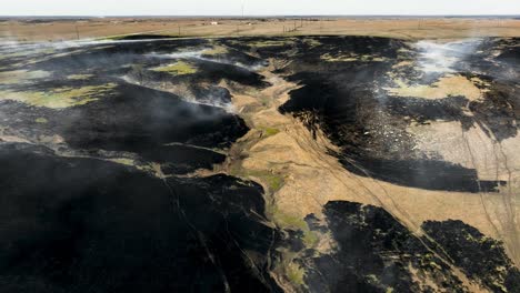 Smoke-blowing-in-the-wind-off-freshly-burnt-prairie-after-controlled-burn-in-the-Flint-Hills-of-Kansas,-Reverse-Drone-Shot