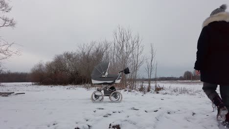 Baby-carriage-on-snowy-countryside-road,-mother-walk-and-continue-activity