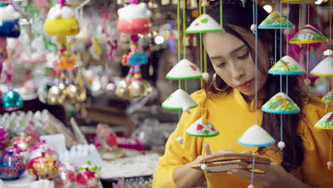 Young-woman-in-yellow-Ao-Dai-admiring-crafts-at-Hoi-An-market,-vibrant-colors,-close-up