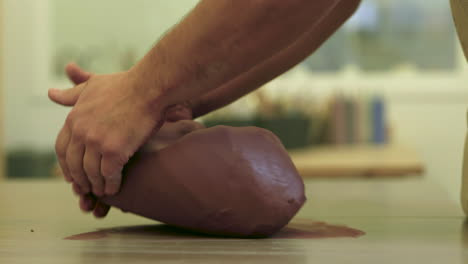 Male-hands-placing-raw-clay-material-onto-studio-work-table-preparing-top-sculpt-block