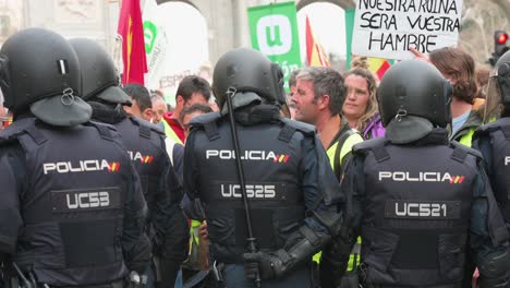 A-police-officer-holds-a-baton-as-they-stand-guard-as-Spanish-farmers-and-agricultural-unions-protest-against-unfair-competition,-agricultural-and-government-policies