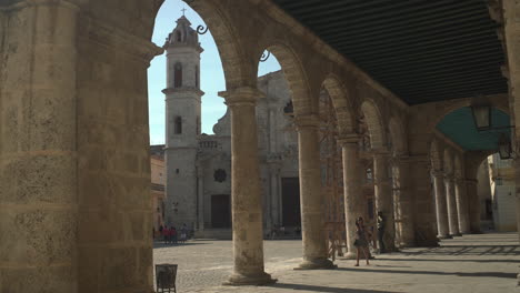 A-unique-angle-of-Plaza-Vieja-offers-a-glimpse-of-the-Havana-Cathedral,-with-a-tourist-strolling-and-appreciating-the-architecture