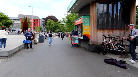 Lone-musician-performs-in-Galway's-Eyre-Square,-passersby-in-the-distance