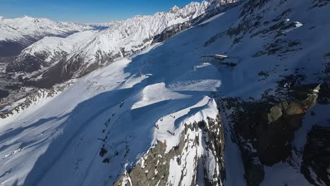 Aerial-view-of-french-Alps,-ski-trail-at-Chamonix-Mont-Blanc-with-skiers-and-mountain-peaks-in-the-distance-on-a-sunny-winter-day