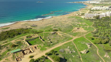 Aerial-view-of-Tombs-of-the-Kings,-Paphos,-with-a-clear-view-of-the-ancient-ruins,-paths,-surrounding-greenery,-and-coastline