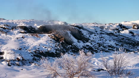 Volcanic-steam-billows-from-a-crater-in-a-snow-covered-landscape-in-Northern-Iceland,-slow-drone-pan