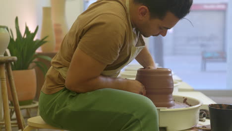 Potter-sitting-working-clay-and-moulding-pottery-on-turntable-in-studio-workshop