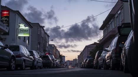 Traveling-cars-pass-by-parked-cars-in-a-street-with-hotels-and-shops---Evening-to-Night-Timelapse-zoom-in