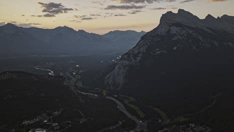 Banff-AB-Canada-Aerial-v8-high-altitude-drone-flyover-town-center-capturing-forested-valley,-Bow-river-course-and-mountain-ranges-at-sunrise-in-the-summer---Shot-with-Mavic-3-Pro-Cine---July-2023