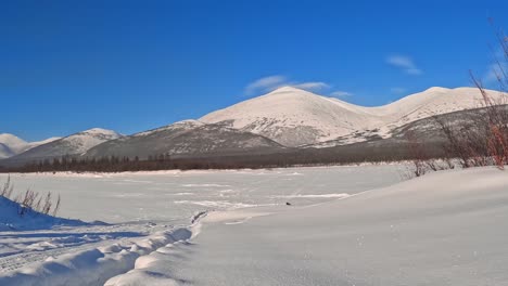 Eintauchen-In-Die-Magie-Der-Winternatur:-Ein-Gefrorener-Fluss-Und-Majestätische-Schneebedeckte-Berge,-Die-In-Wolken-Gehüllt-Sind