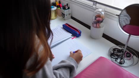 Over-the-shoulder-view-of-a-girl-writing-in-a-notebook,-4K