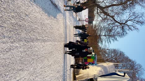 People-walk-on-snowy-sunny-day-by-river-in-Stockholm,-vertical-shot